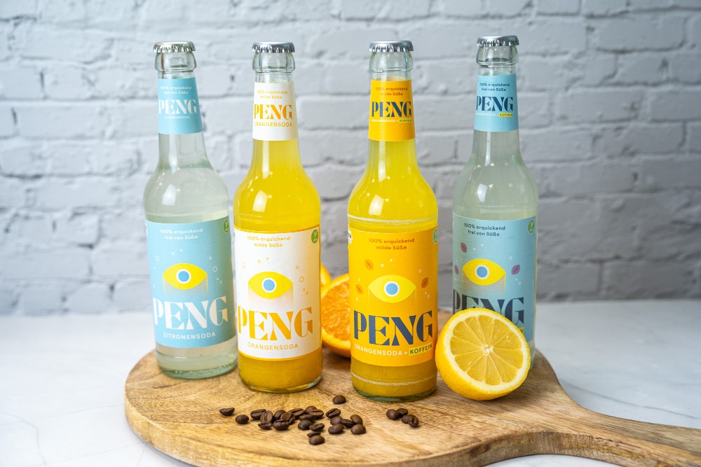Abbildung: Vier Flaschen der Firma Peng stehen auf einem Servierbrett. Daneben liegen eine aufgeschnittene Orange und Kaffeebohnen.