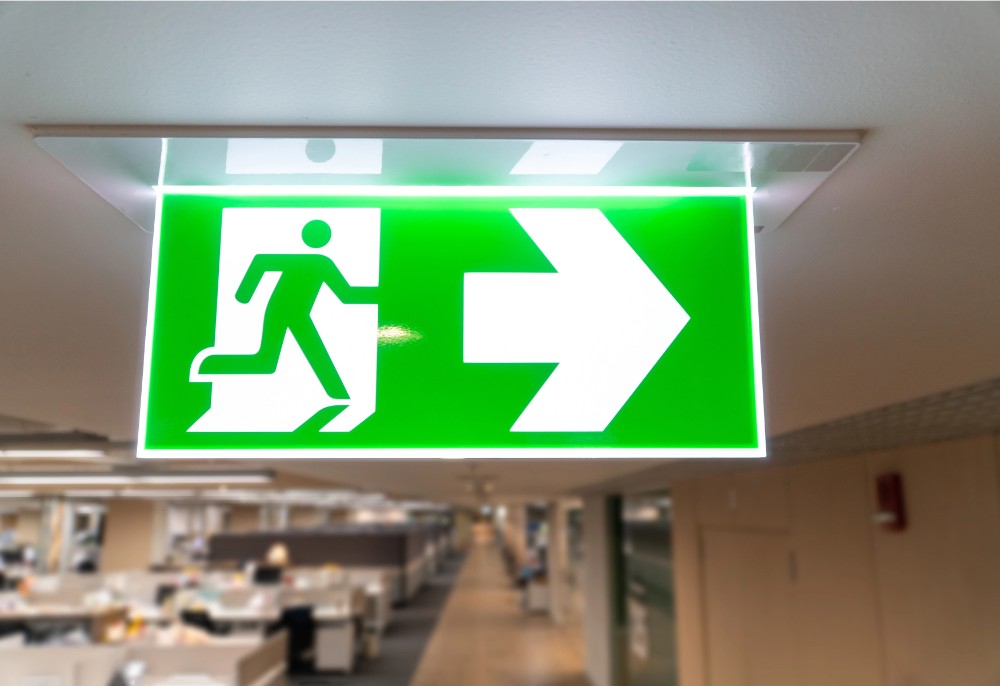 Ein Leuchtendes Fluchtwegschild im Bürogebäude zeigt den Weg zum Notausgang. Abbildung: Prot Tachapanit, Depositphotos